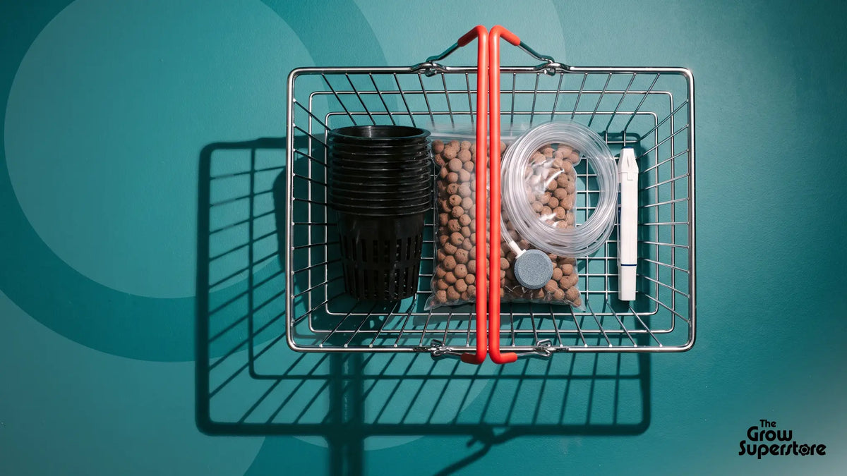 Overhead view of a red-handled shopping basket holding net pots, clay pebbles, air tubing with air stone and a pH pen on teal