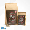 Two bags of Ecothrive Soil Food Bloom (5 kg and 1 kg) standing side by side with a pile of light‑brown powder in front – thegrowsuperstore.com